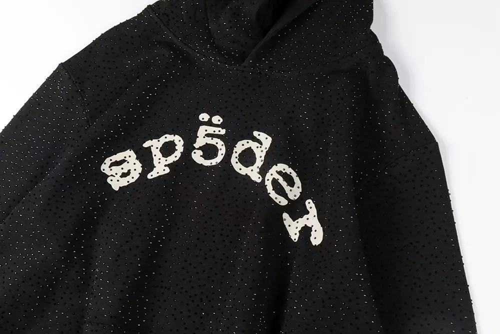 A detailed close-up of the Sp5der logo on the chest of the Sp5der VVS Hoodie in Black, showcasing the main design and rhinestone craftsmanship details.A detailed close-up of the Sp5der logo on the chest of the Sp5der VVS Hoodie in Black, showcasing the main design and rhinestone craftsmanship details.
