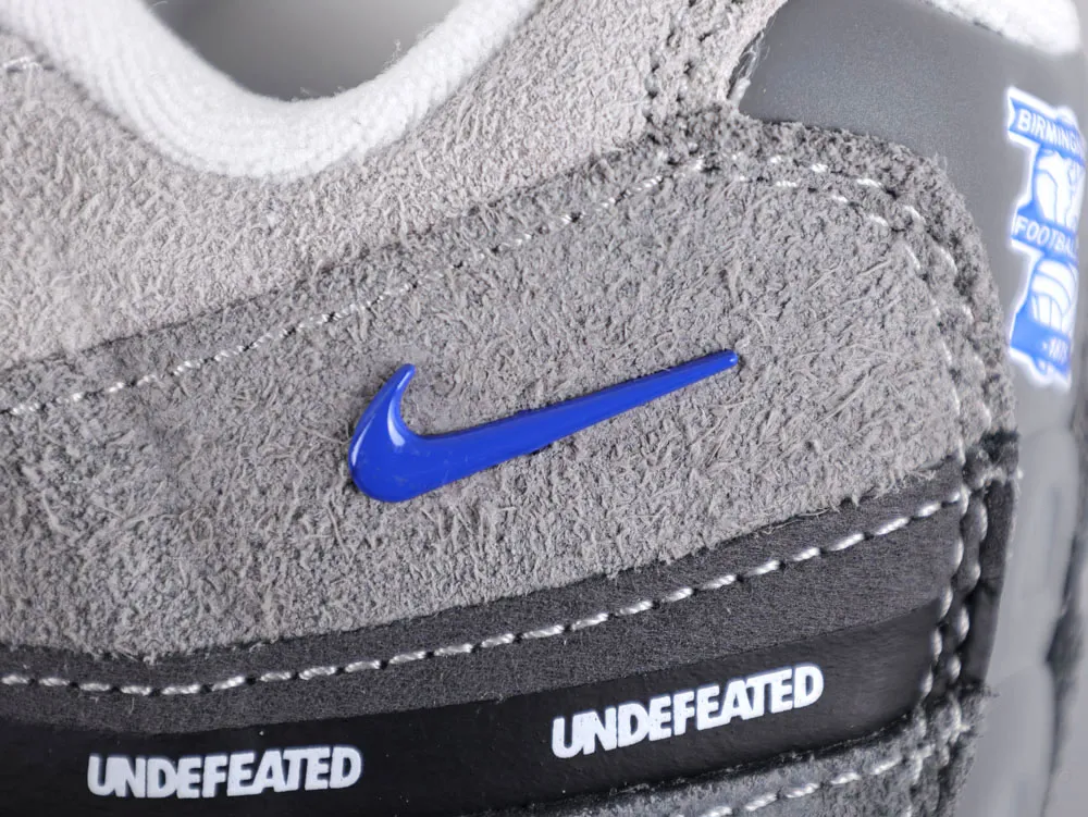 Gray suede sneaker with a blue logo and black leather detailing near sole.