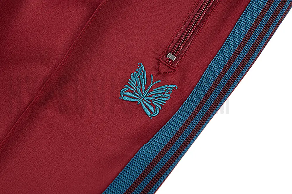Close-up detail of the track pants pocket and delicate butterfly embroidery.