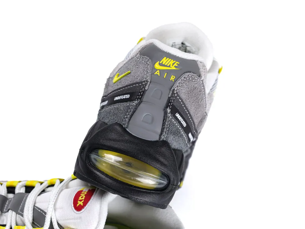 Gray and black sneaker with suede and leather, featuring yellow accents and air cushion.