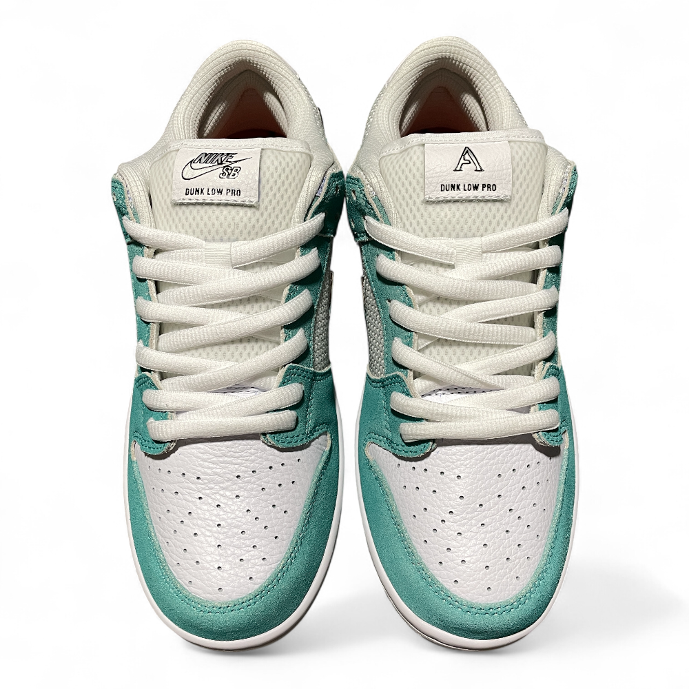Close-up of a sneaker's tongue in white mesh, with teal suede accents and white laces crossing diagonally.
