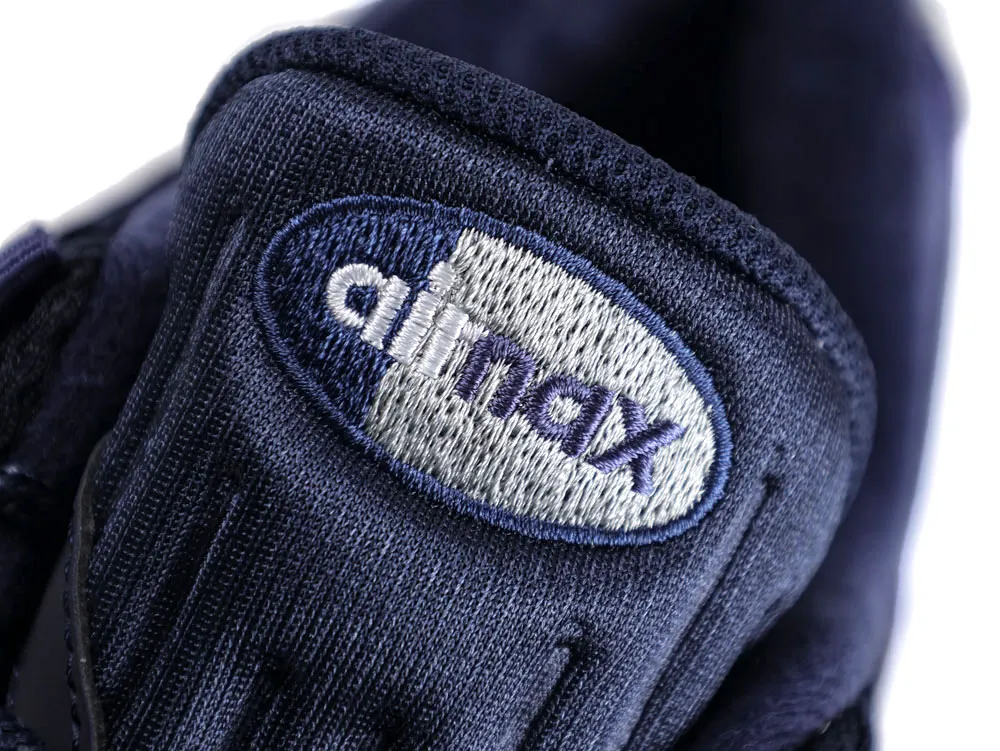 Close-up of navy blue fabric sneaker tongue with embroidered logo.