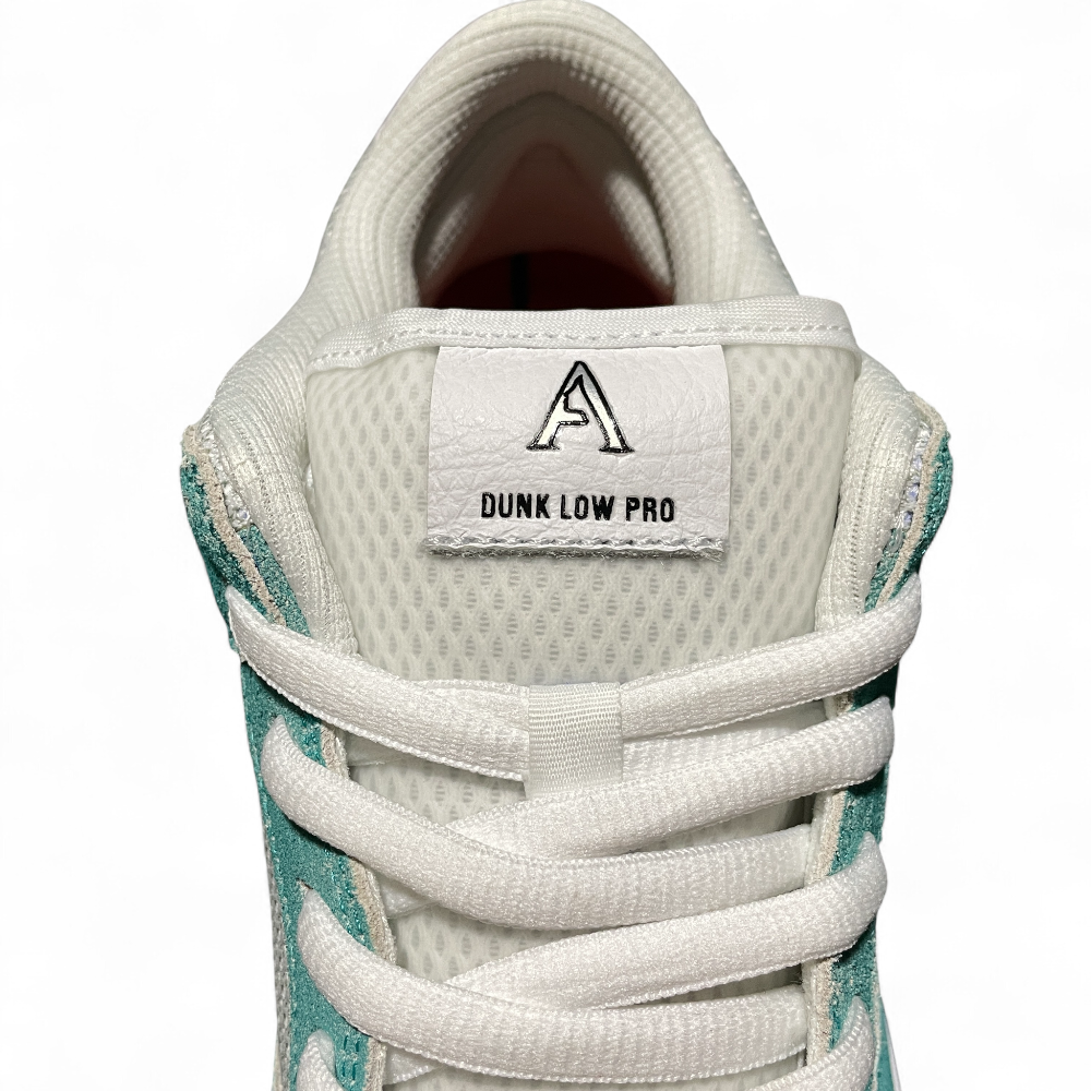 Close-up of a sneaker's tongue with white mesh material, teal suede accents, and flat white laces crossing diagonally.