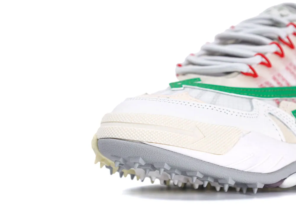 Close-up of sneaker with white leather upper, green accents, and spiked gray sole.
