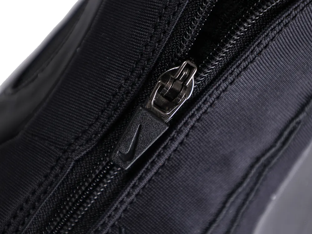 Close-up of a black fabric zipper with a metal puller on a bag.