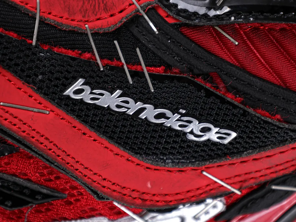 Close-up of a red and black textured fabric shoe with metal needles.
