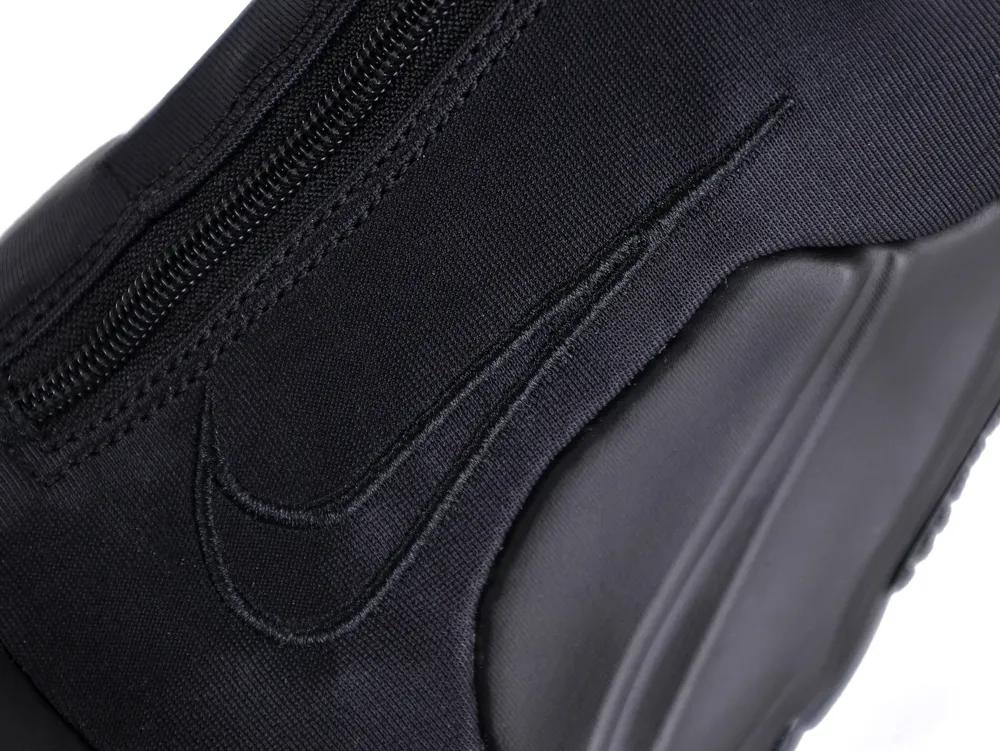 Close-up of a black fabric shoe with a rubber outsole, featuring a side zipper.