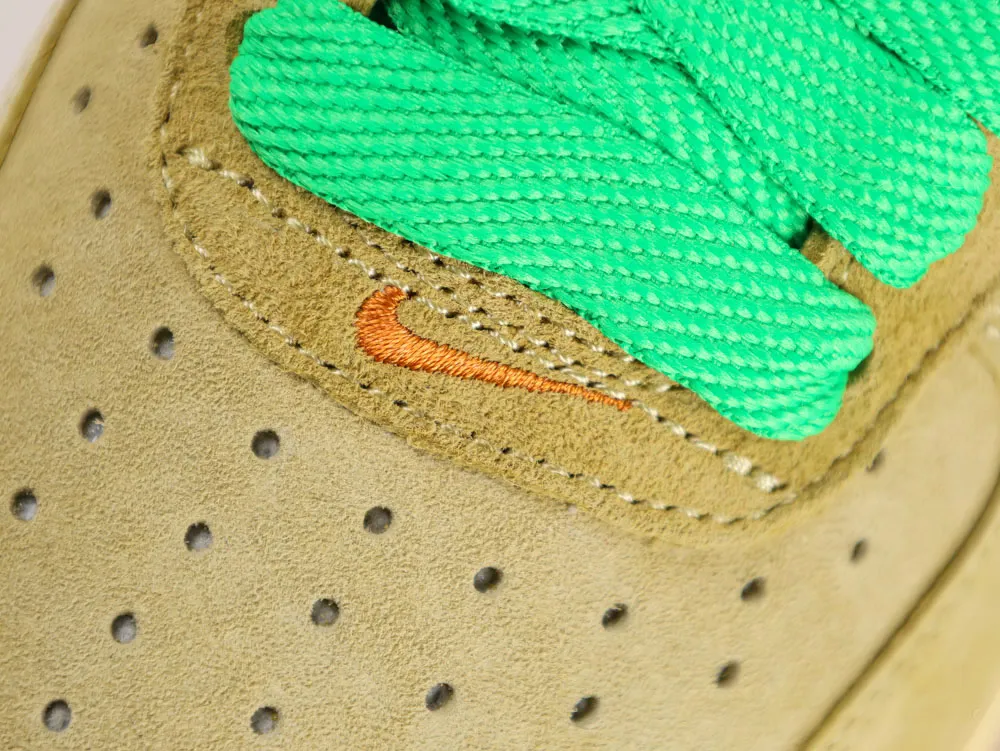 Tan suede shoe with green laces and embroidered orange logo detail.